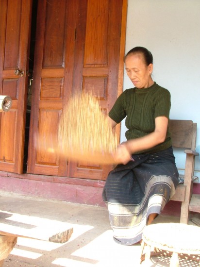 Laos: Mekong River woman husking grain Xieng Maen village by Vincent Ross