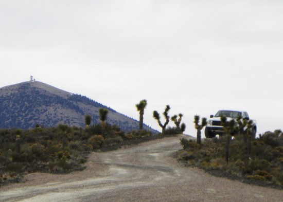 Men in black (?) in white Ford truck, lower right; with Area 51 look out tower on mountain in upper left.